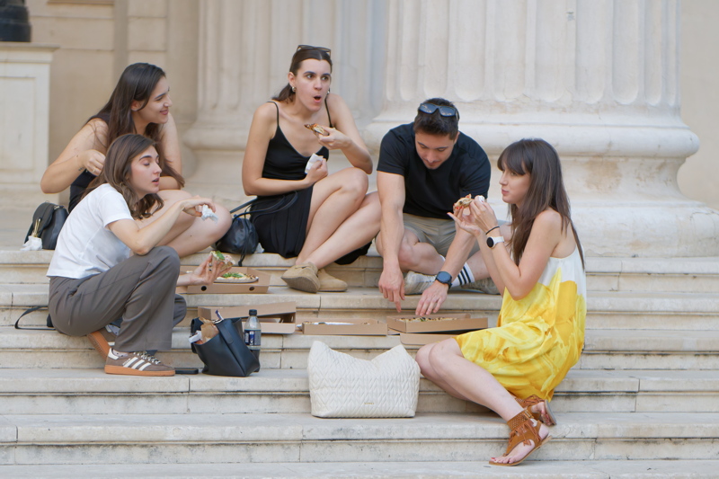 coming_soon_4 - A group of people enjoying pizza on stone steps
